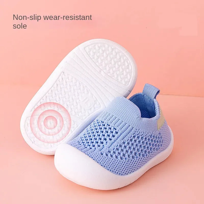 Blue baby shoe with white sole on a pink background, highlighting non-slip feature.