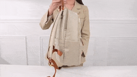 Video of woman displaying an ivory luxurious backpack and its features in a white room
