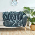 Gray blanket draped over a beige sofa in a living room with a clock and plant in the background.
