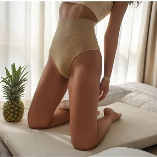 Person wearing beige high-waisted shapewear sitting on a bed with a pineapple next to them.