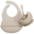 Beige silicone baby bib, bowl, and soft spoon tableware set on a white background