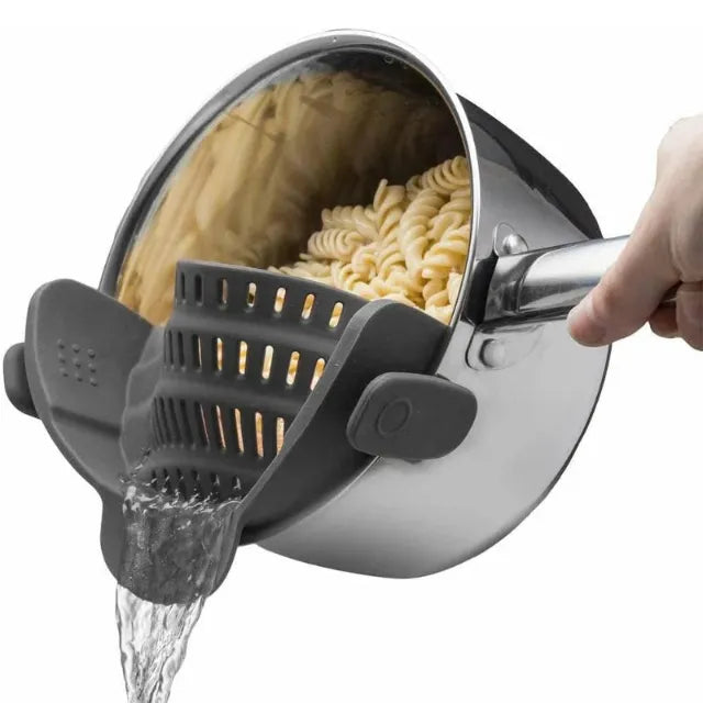 Pasta being drained with a gray silicone strainer from a steel pot on white background